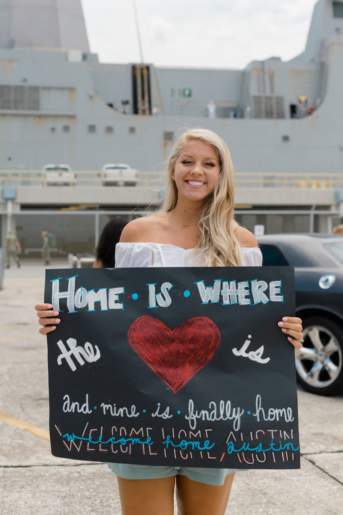 military wife holding a welcome home sign for her husband at a homecoming